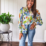 Bright green, orange and blue florals adorn this white button down blouse with a collar, puff sleeves and white eyelet trim throughout.
