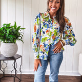 Bright green, orange and blue florals adorn this white button down blouse with a collar, puff sleeves and white eyelet trim throughout.