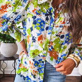 Bright green, orange and blue florals adorn this white button down blouse with a collar, puff sleeves and white eyelet trim throughout.