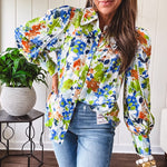 Bright green, orange and blue florals adorn this white button down blouse with a collar, puff sleeves and white eyelet trim throughout.