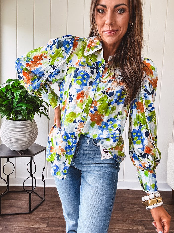 Bright green, orange and blue florals adorn this white button down blouse with a collar, puff sleeves and white eyelet trim throughout.