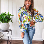 Bright green, orange and blue florals adorn this white button down blouse with a collar, puff sleeves and white eyelet trim throughout.