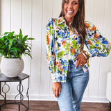 Bright green, orange and blue florals adorn this white button down blouse with a collar, puff sleeves and white eyelet trim throughout.