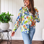 Bright green, orange and blue florals adorn this white button down blouse with a collar, puff sleeves and white eyelet trim throughout.