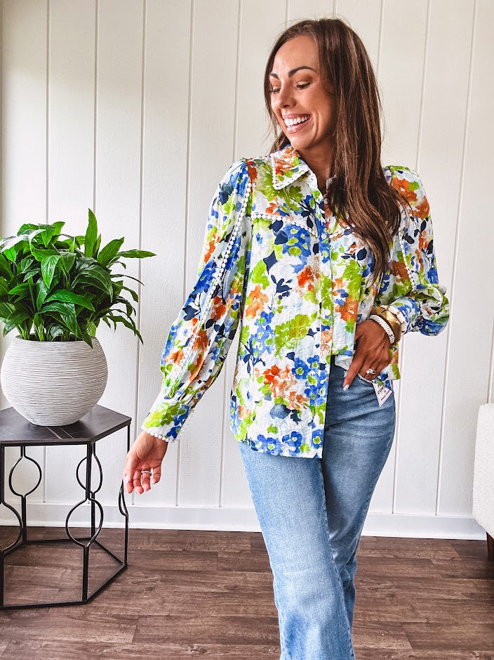 Bright green, orange and blue florals adorn this white button down blouse with a collar, puff sleeves and white eyelet trim throughout.
