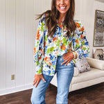 Bright green, orange and blue florals adorn this white button down blouse with a collar, puff sleeves and white eyelet trim throughout.