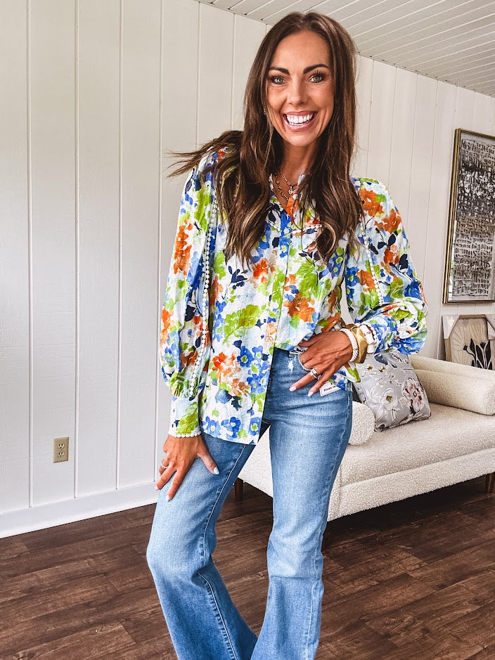 Bright green, orange and blue florals adorn this white button down blouse with a collar, puff sleeves and white eyelet trim throughout.