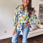 Bright green, orange and blue florals adorn this white button down blouse with a collar, puff sleeves and white eyelet trim throughout.