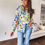 Bright green, orange and blue florals adorn this white button down blouse with a collar, puff sleeves and white eyelet trim throughout.
