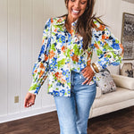 Bright green, orange and blue florals adorn this white button down blouse with a collar, puff sleeves and white eyelet trim throughout.