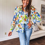 Bright green, orange and blue florals adorn this white button down blouse with a collar, puff sleeves and white eyelet trim throughout.