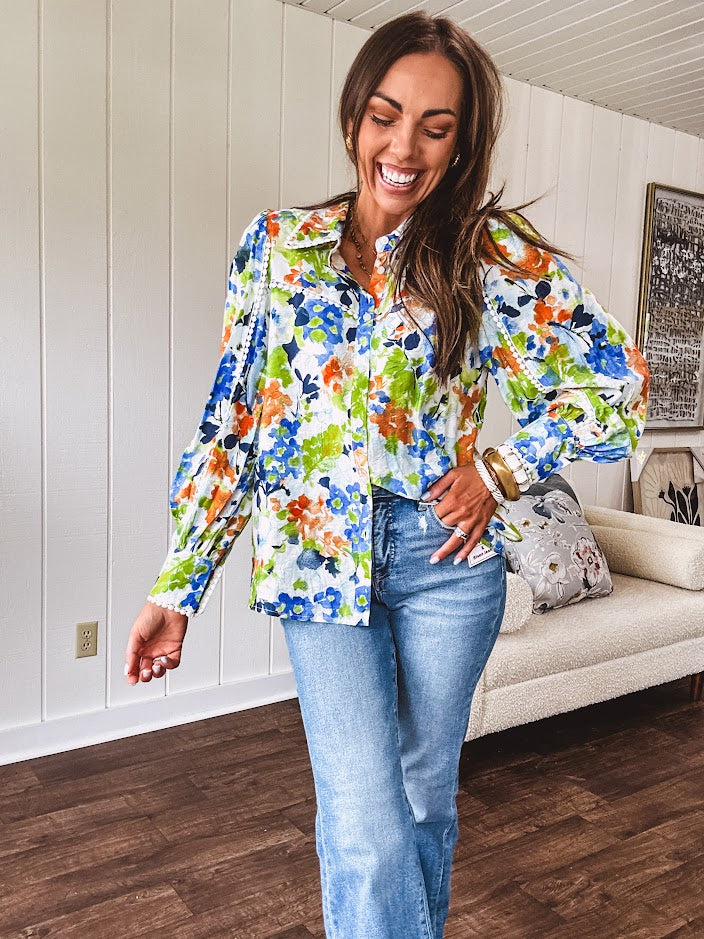 Bright green, orange and blue florals adorn this white button down blouse with a collar, puff sleeves and white eyelet trim throughout.