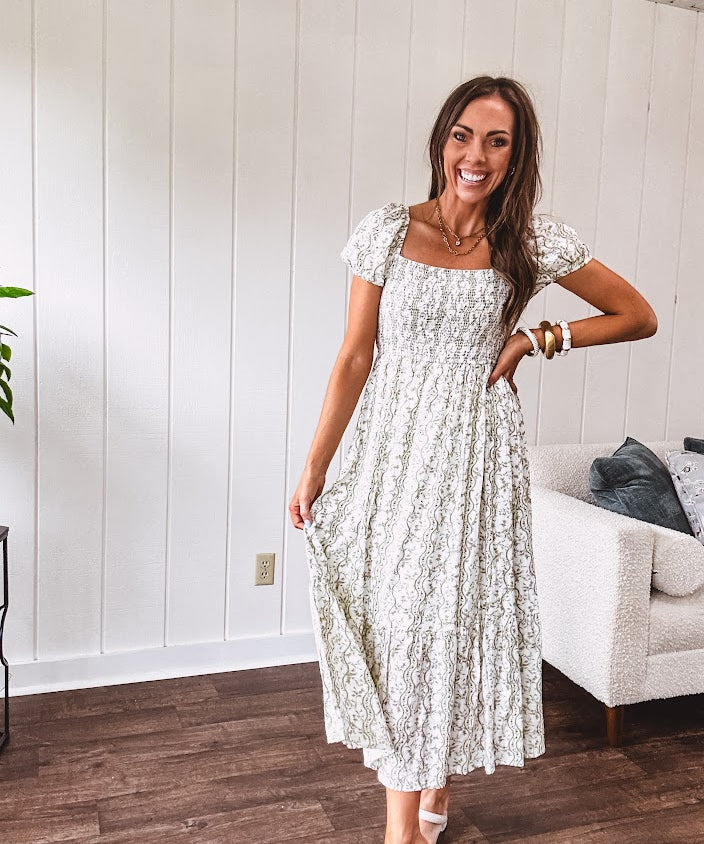 White dress with green dainty vines print, capped elastic sleeves and elastic square neckline, smocked bodice and tiered, fully lined skirt.