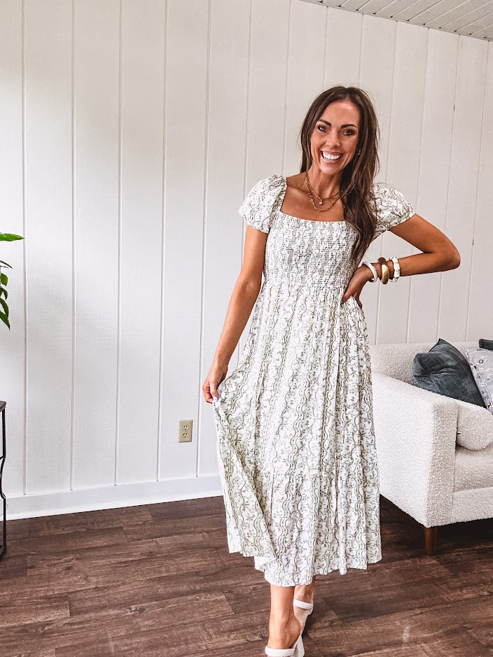 White dress with green dainty vines print, capped elastic sleeves and elastic square neckline, smocked bodice and tiered, fully lined skirt.