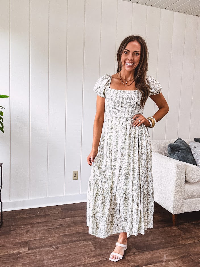 White dress with green dainty vines print, capped elastic sleeves and elastic square neckline, smocked bodice and tiered, fully lined skirt.