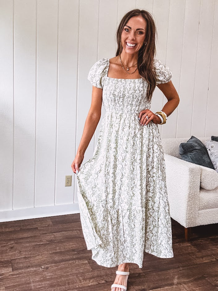 White dress with green dainty vines print, capped elastic sleeves and elastic square neckline, smocked bodice and tiered, fully lined skirt.