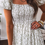 White dress with green dainty vines print, capped elastic sleeves and elastic square neckline, smocked bodice and tiered, fully lined skirt.