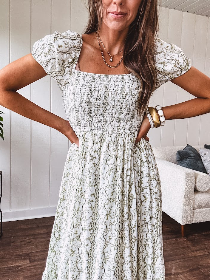 White dress with green dainty vines print, capped elastic sleeves and elastic square neckline, smocked bodice and tiered, fully lined skirt.