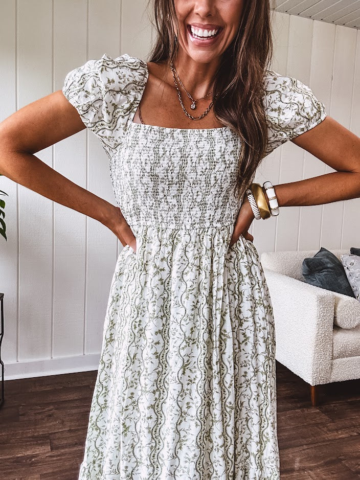 White dress with green dainty vines print, capped elastic sleeves and elastic square neckline, smocked bodice and tiered, fully lined skirt.