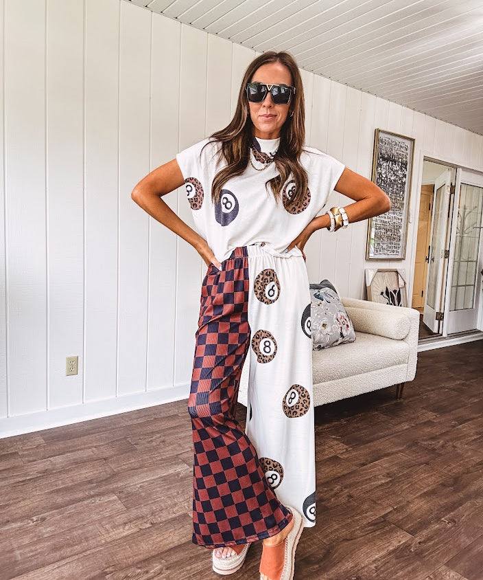 Soft, flowy wide leg pants with elastic waist, pockets and one leg featuring rust and black checks and the other cream with leo and black 8 ball motif.
