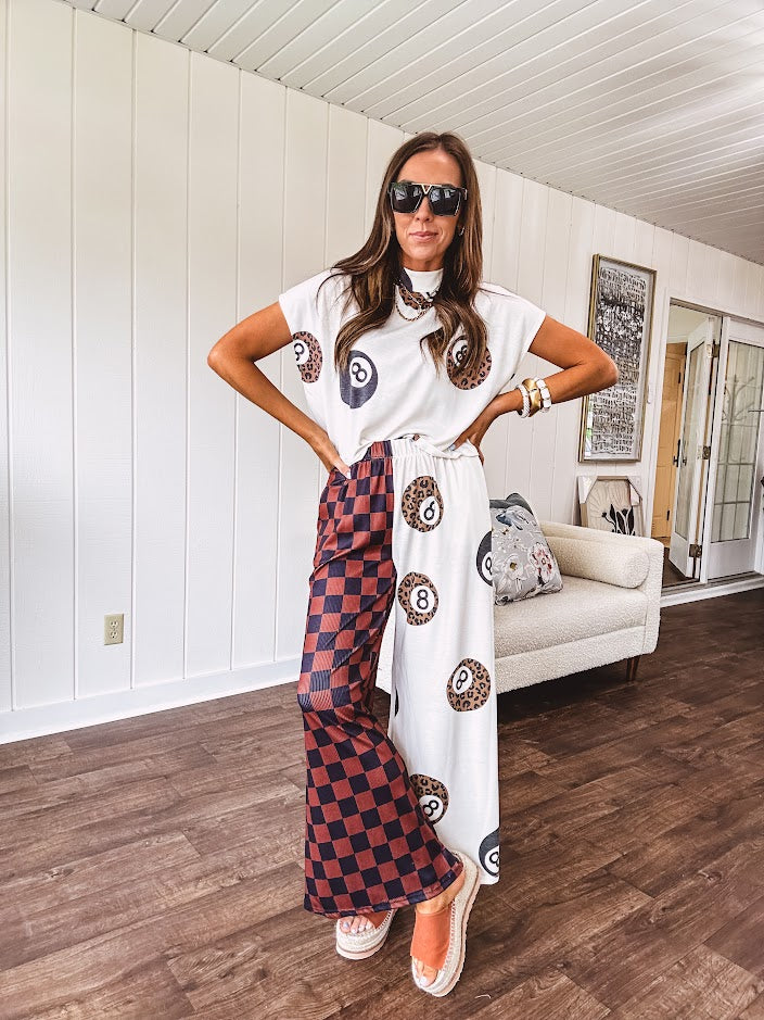 Soft, flowy wide leg pants with elastic waist, pockets and one leg featuring rust and black checks and the other cream with leo and black 8 ball motif.