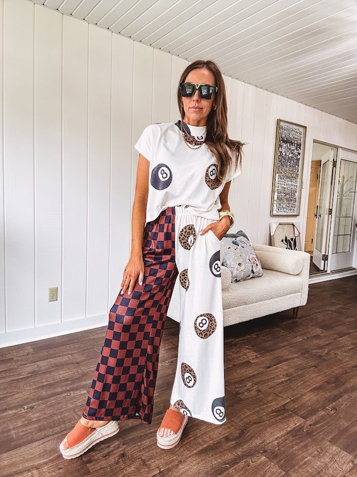 Soft, flowy wide leg pants with elastic waist, pockets and one leg featuring rust and black checks and the other cream with leo and black 8 ball motif.