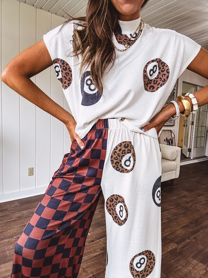 Soft, flowy wide leg pants with elastic waist, pockets and one leg featuring rust and black checks and the other cream with leo and black 8 ball motif.