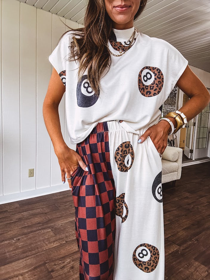 Soft, flowy wide leg pants with elastic waist, pockets and one leg featuring rust and black checks and the other cream with leo and black 8 ball motif.