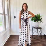 Maxi length ivory and black polka dot button front dress with collar, matching black waist tie and sleeveless design.