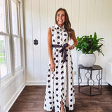 Maxi length ivory and black polka dot button front dress with collar, matching black waist tie and sleeveless design.