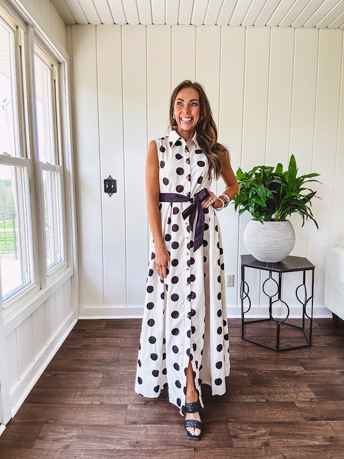Maxi length ivory and black polka dot button front dress with collar, matching black waist tie and sleeveless design.