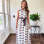 Maxi length ivory and black polka dot button front dress with collar, matching black waist tie and sleeveless design.