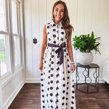 Maxi length ivory and black polka dot button front dress with collar, matching black waist tie and sleeveless design.
