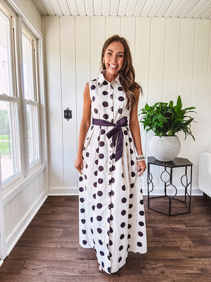 Maxi length ivory and black polka dot button front dress with collar, matching black waist tie and sleeveless design.