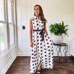 Maxi length ivory and black polka dot button front dress with collar, matching black waist tie and sleeveless design.