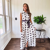 Maxi length ivory and black polka dot button front dress with collar, matching black waist tie and sleeveless design.