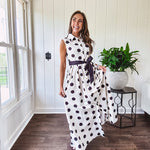 Maxi length ivory and black polka dot button front dress with collar, matching black waist tie and sleeveless design.