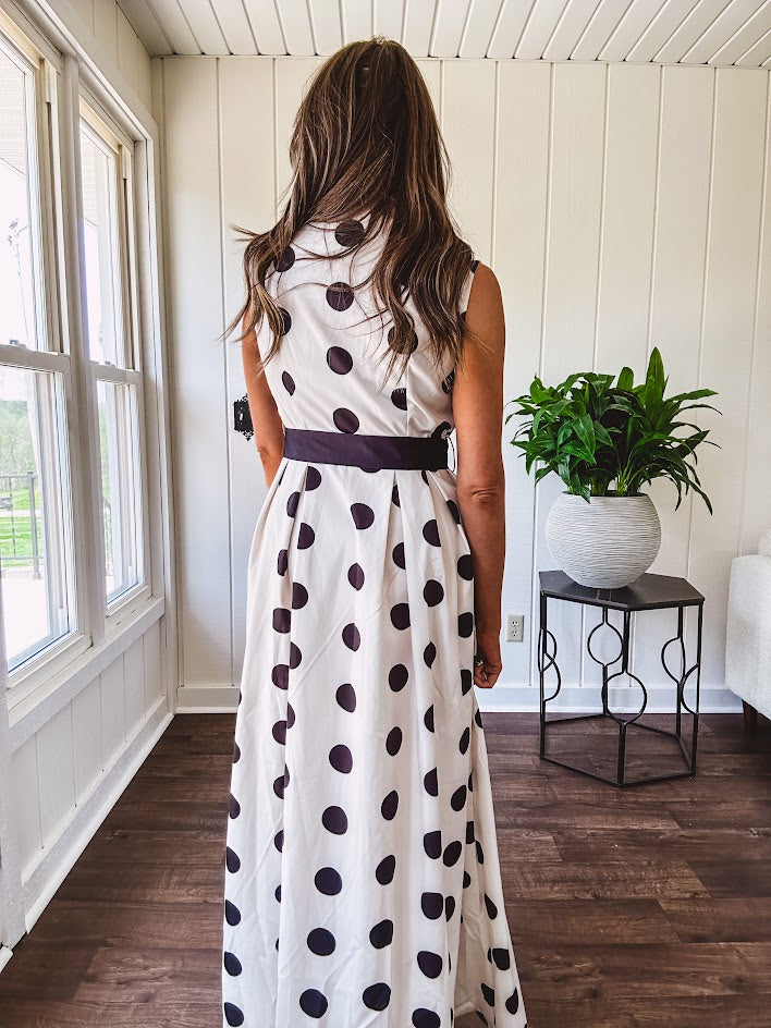 Maxi length ivory and black polka dot button front dress with collar, matching black waist tie and sleeveless design.