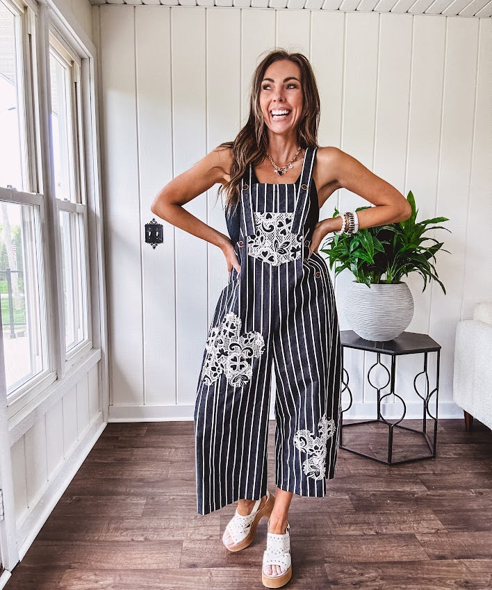 Thin, lightweight black and ivory striped overalls featuring black and ivory lace crochet patches throughout and faux wooden buttons at the adjustable straps and sides.