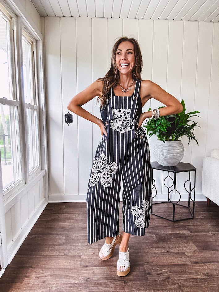 Thin, lightweight black and ivory striped overalls featuring black and ivory lace crochet patches throughout and faux wooden buttons at the adjustable straps and sides.