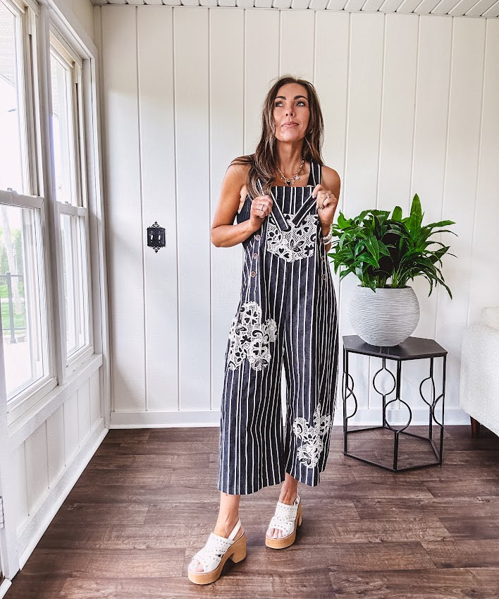 Thin, lightweight black and ivory striped overalls featuring black and ivory lace crochet patches throughout and faux wooden buttons at the adjustable straps and sides.