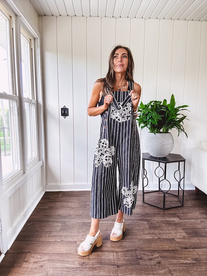 Thin, lightweight black and ivory striped overalls featuring black and ivory lace crochet patches throughout and faux wooden buttons at the adjustable straps and sides.