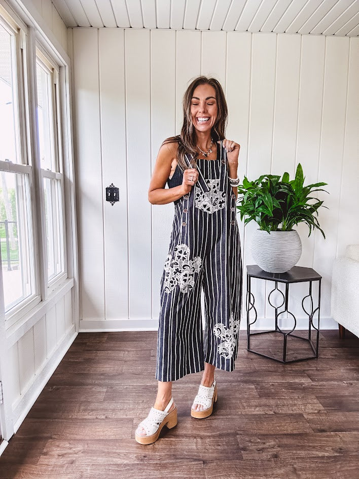 Thin, lightweight black and ivory striped overalls featuring black and ivory lace crochet patches throughout and faux wooden buttons at the adjustable straps and sides.