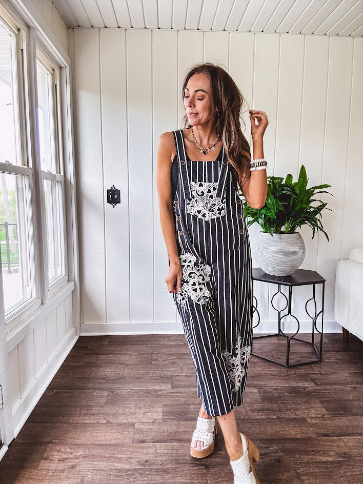 Thin, lightweight black and ivory striped overalls featuring black and ivory lace crochet patches throughout and faux wooden buttons at the adjustable straps and sides.