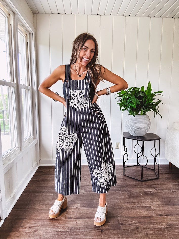 Thin, lightweight black and ivory striped overalls featuring black and ivory lace crochet patches throughout and faux wooden buttons at the adjustable straps and sides.