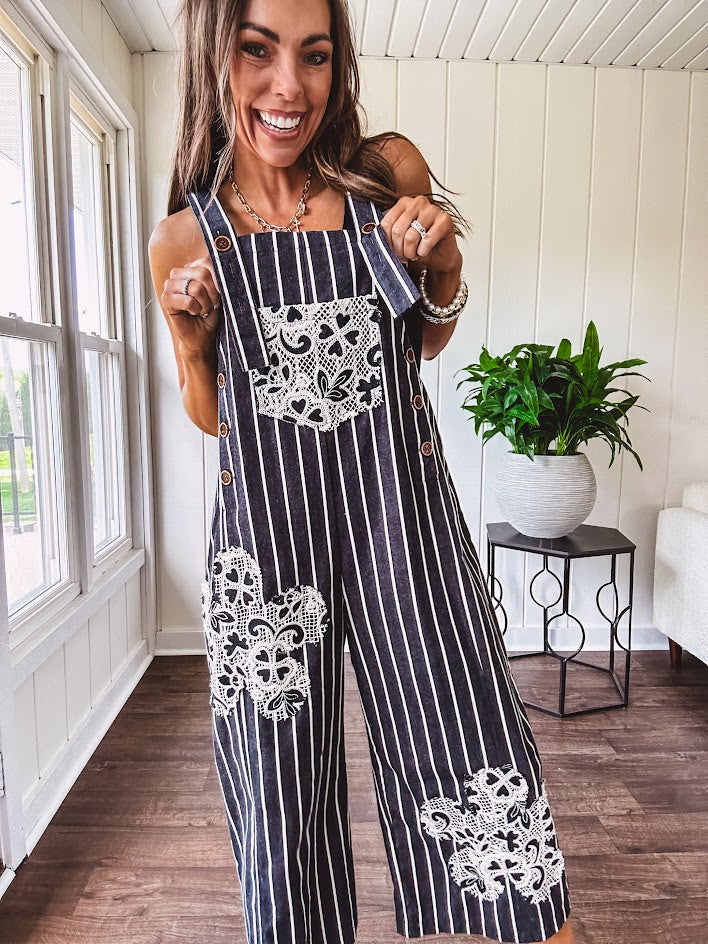 Thin, lightweight black and ivory striped overalls featuring black and ivory lace crochet patches throughout and faux wooden buttons at the adjustable straps and sides.