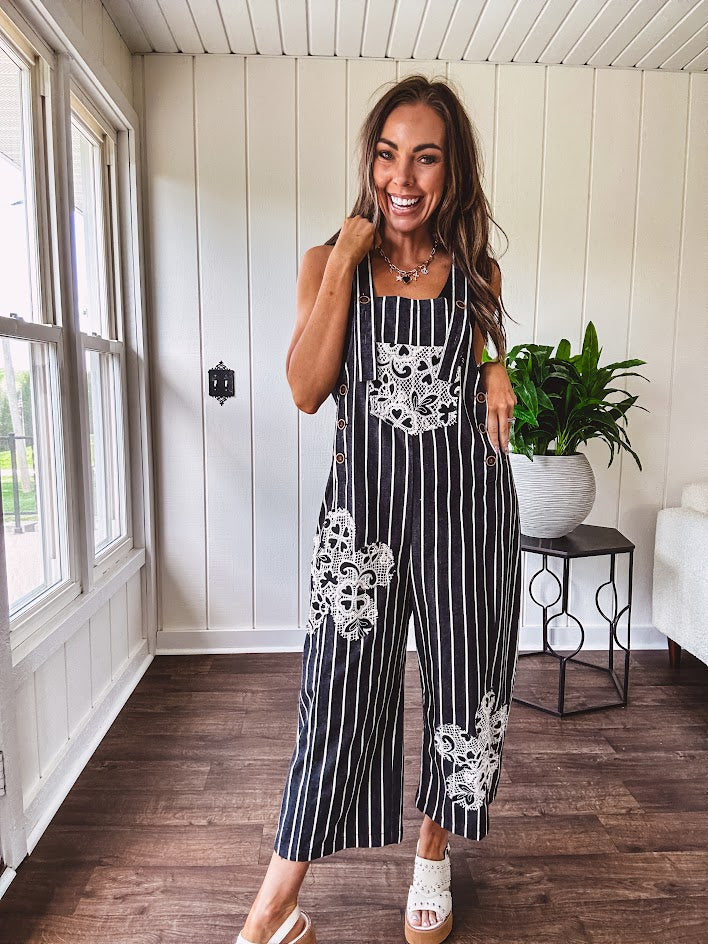Thin, lightweight black and ivory striped overalls featuring black and ivory lace crochet patches throughout and faux wooden buttons at the adjustable straps and sides.