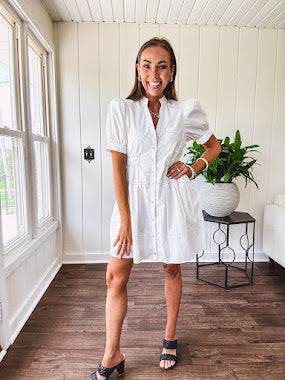 Fully lined white button down front dress with mock neck, V neck, short puffed sleeves, front pocket and elastic bands at the waist for a cinched waist look.