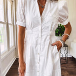 Fully lined white button down front dress with mock neck, V neck, short puffed sleeves, front pocket and elastic bands at the waist for a cinched waist look.
