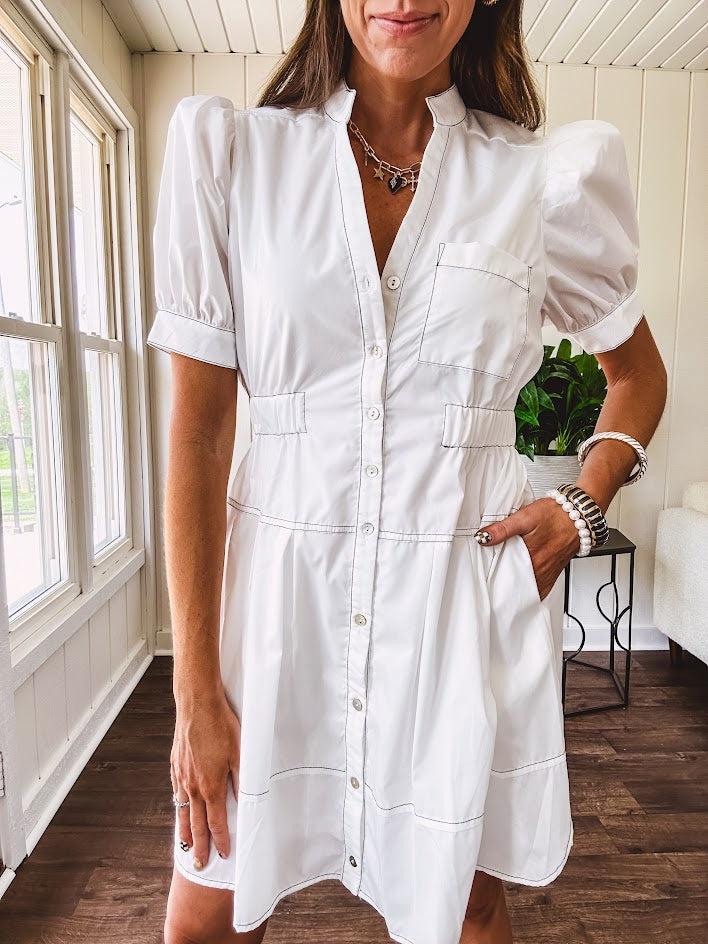 Fully lined white button down front dress with mock neck, V neck, short puffed sleeves, front pocket and elastic bands at the waist for a cinched waist look.